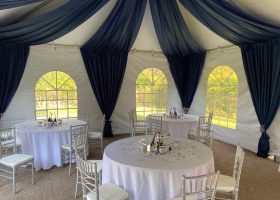 WHITE FRAME TENT WITH CATHEDRAL SIDEWALLS AND BLUE MOON TAFFETA SWAGGING AND LEG DRAPES WITH SILVER CHIAVARI CHAIRS